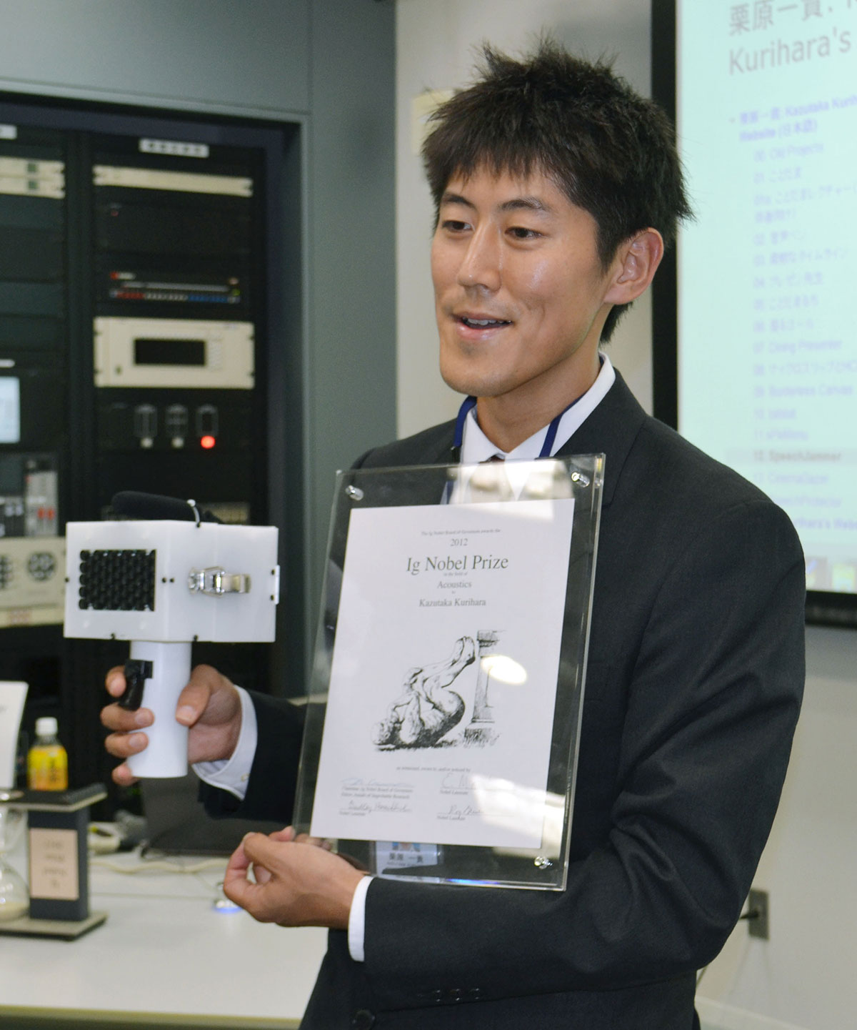 「スピーチ・ジャマー」の試作品を手に記者会見する栗原一貴教授。 「酔った人に試したい」と語っていた(写真・共同通信)