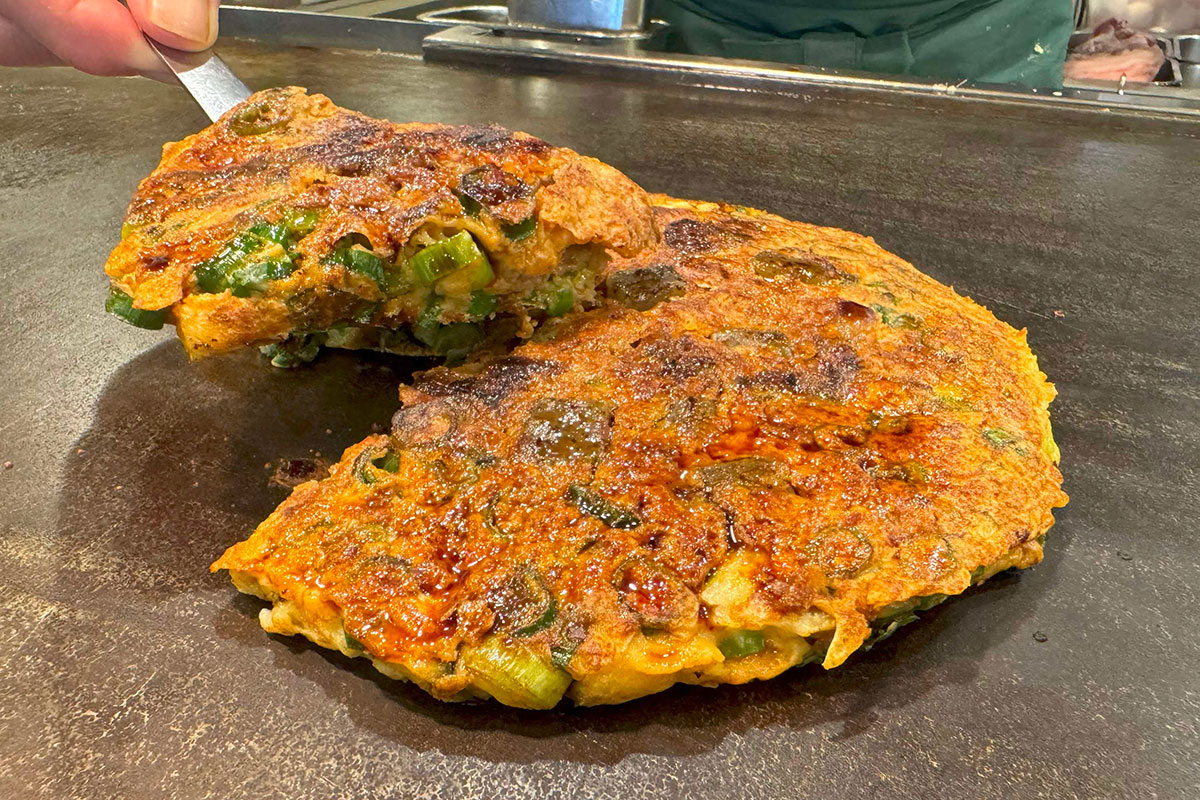 【ねぎ焼 やまもと】JR新大阪駅新幹線改札内 大阪のれんめぐり・営業時間／10:00～21:30（L.O. 21:10）定休日／施設に準じる。山盛りの青ねぎをふんだんに使って焼き上げるねぎ焼きは、甘辛く炊いた牛すじとこんにゃくが相性抜群。仕上げに特製しょう油だれとレモンを絞ってあっさりと食べられる。新幹線の待ち時間に、本場の味を堪能できる一皿だ。