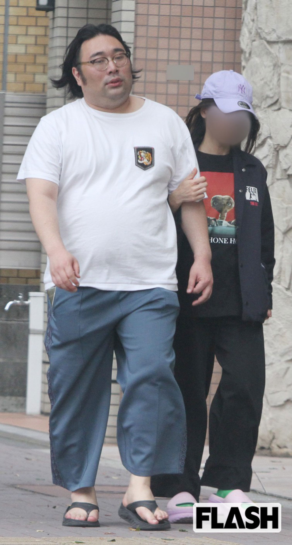 2026年5月、妻のA子さんと一緒にパチンコ店を出たビスケットブラザーズ・原田泰雅。大通りの交差点では人目を気にしてか、数歩離れて信号を待っていたが、人通りが少なくなると、おもむろにA子さんが原田の腕に手を回して、体を寄せ合っていた。寡黙のイメージが強い原田だが、ときおり見つめ合ったり、笑いあったりと幸せそうな様子だ（写真・金谷千治）