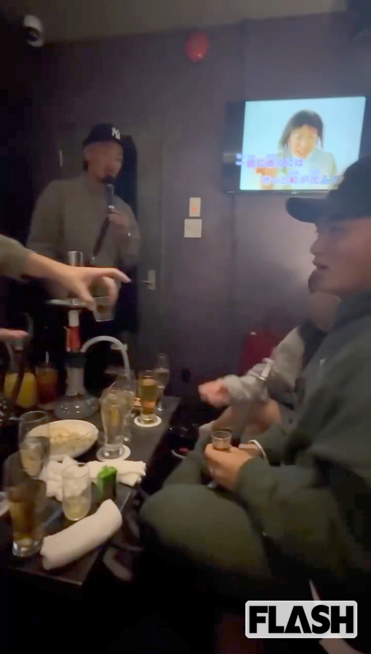 矢野（左奥）が『ハナミズキ』を歌うなか、テレビマンが田村（右）に酒を手渡そうとしている